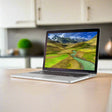 A silver Apple MacBook Pro 2015 A1502 i5 5257U 2.7GHz 8GB 256GB SSD 13.3" by Apple sits on a light kitchen table, its Retina Display showing green hills, a winding river, and snow-capped mountains.