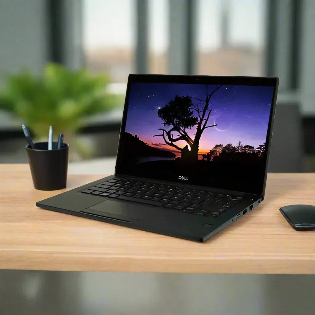 A Dell Latitude E7280 i7 7600U 2.8GHz 16GB 256GB WWAN 12.5 Touch W10P laptop sits on a wooden desk displaying a sunset, with a black pen cup and wireless mouse nearby; blurred green plant and windows are in the background.