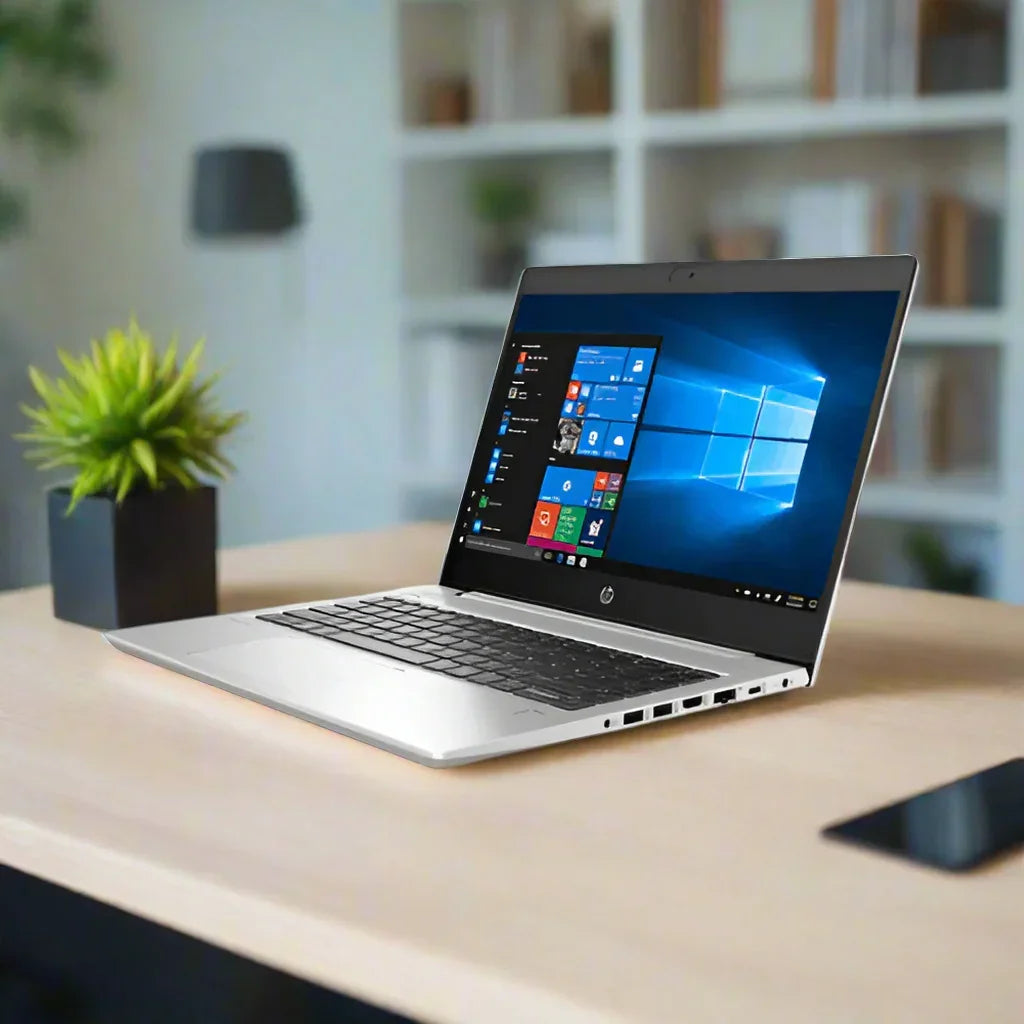 A silver HP ProBook 440 G7 with a 10th Gen Intel Core i5, 8GB RAM, and 256GB SSD is open on a wooden desk, displaying Windows and surrounded by a potted plant and smartphone. This certified refurbished HP laptop includes warranty.