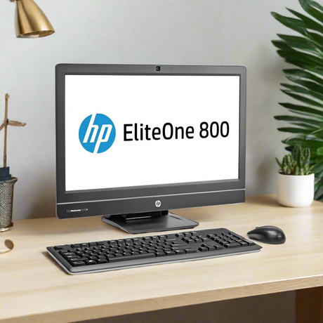 An HP EliteOne 800 G1 AIO i7 desktop with 8GB RAM, 1TB HDD, and a 23 display sits on a light wood desk with keyboard and mouse. The HP logo is on screen; plants and office supplies are in the background.