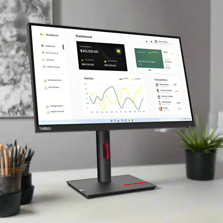 A refurbished Lenovo ThinkVision T23i-30 IPS 23" 1920x1080 monitor displays a financial dashboard with balances, stats graphs, and transactions. The standless Lenovo monitor rests on a desk with pen and pencil cups nearby.
