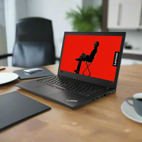 A certified refurbished Lenovo ThinkPad T480 i5 8350U 1.7GHz 24GB 256GB SSD W11P 14" Touch laptop sits open on a wooden desk, surrounded by a cup, saucer, and office supplies. A red screen with a silhouette is displayed.
