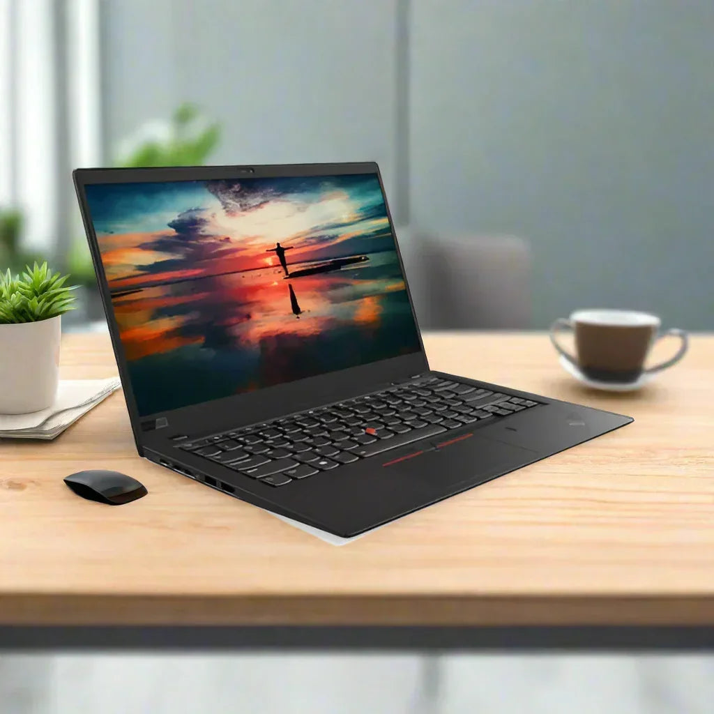 A certified refurbished Lenovo ThinkPad X1 Carbon G5 i5 6200U 2.3GHz 8GB 256GB 14" W10P sits on a wooden desk, displaying a vibrant sunset over water, with a black wireless mouse, potted plant, and cup in the softly blurred background.