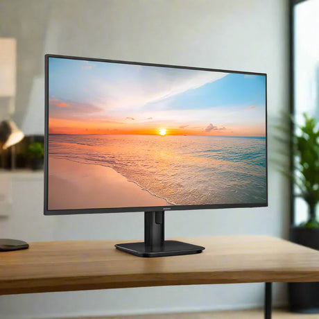 A Philips 27E1N1100D 27" IPS monitor, without a stand, displays a vivid beach sunset with calm waves on a wooden desk. A blurred plant and softly lit modern decor appear in the background.