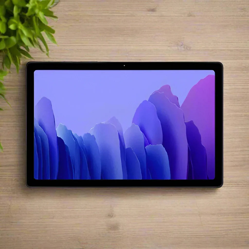 A certified refurbished Samsung Galaxy Tab A7 SM-T505 32GB Tablet Black by Samsung rests on a light wooden surface beside a green leafy plant, displaying a purple and blue abstract wallpaper.