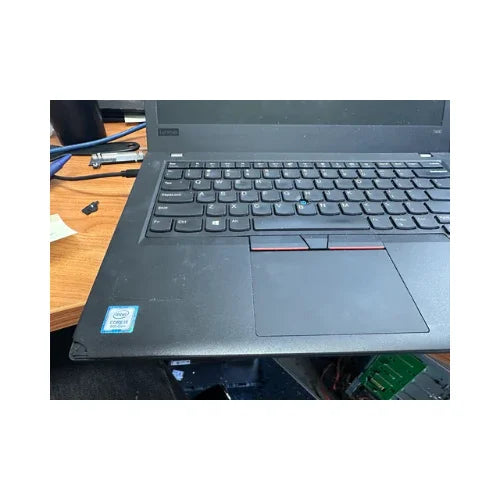 A close-up of an open Lenovo ThinkPad T480 i5 8250U 16GB 256GB SSD 14", showing part of the keyboard, touchpad, and Intel Core i5 sticker on a wooden desk. Cables and a USB drive appear in the background.