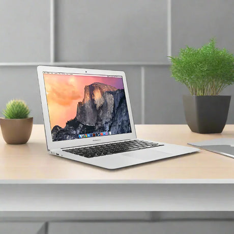 A silver Apple MacBook Air 2017 A1466 i5 1.8GHz 8GB 256GB 13.3" sits on a light wooden desk next to two potted plants and a closed notebook in a modern, minimal office setting.