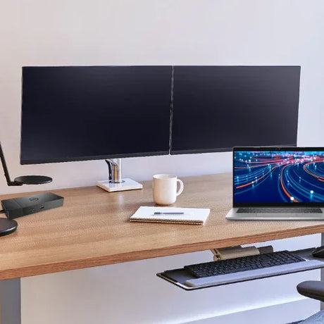 The Reboot IT Office Bundle features a Latitude 5320 i5 laptop, dual 22 monitors, dock, and mount on a modern desk with a pull-out keyboard tray, notebook, white mug, lamp, and the laptop displaying vivid light trails.