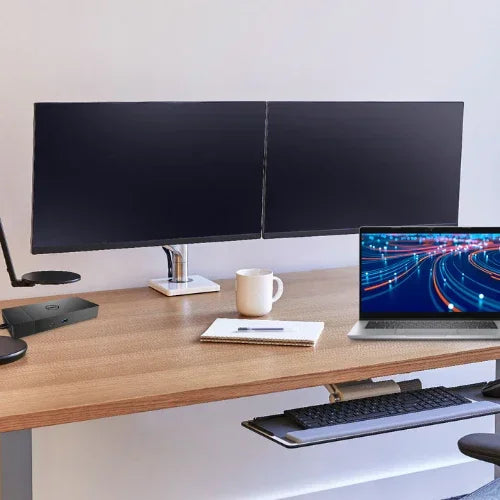 The Reboot IT Office Bundle features a Latitude 5320 i5 laptop, dual 22 monitors, dock, and mount on a modern desk with a pull-out keyboard tray, notebook, white mug, lamp, and the laptop displaying vivid light trails.