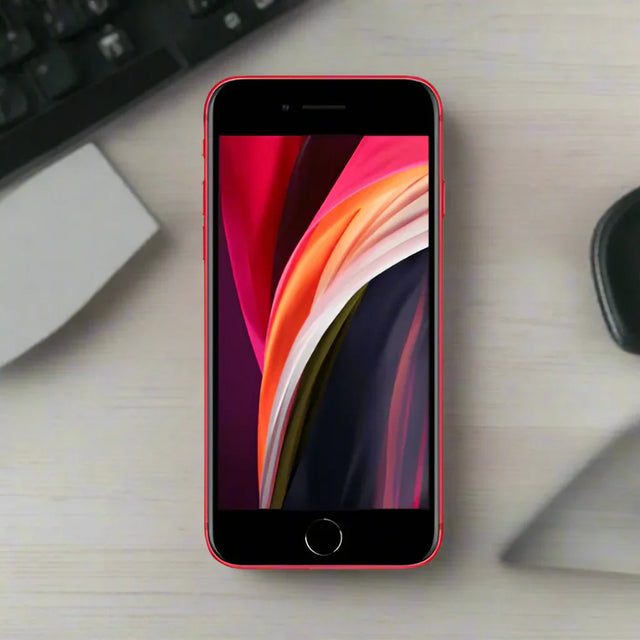 A certified refurbished Apple iPhone SE 2nd Gen 64GB Red (Unlocked, AU STOCK) rests on a light wooden desk near a keyboard, paper, and black object, displaying a vibrant abstract wallpaper. Brand: Apple.