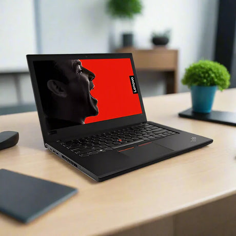 A black Lenovo ThinkPad T480 i7 8650U 16GB 512GB SSD W11P laptop sits on a wooden desk, its screen displaying a man’s profile shouting against a red background; nearby are a plant, blurred items, and shelves in the background.