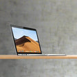 A certified refurbished Apple MacBook Pro 2017 A1708 (13.3", i5 7360U, 8GB RAM, 256GB SSD) displays a vivid desert landscape on its Retina screen as it sits open on a wooden surface against a gray background, with ports and keyboard partly visible.