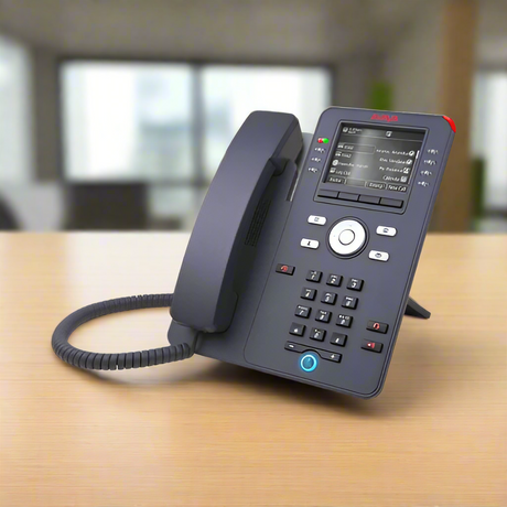 An Avaya J169 IP PoE Desk Phone by Avaya, featuring a digital display, rests on a wooden table in a bright office, delivering unified communication solutions against blurred window backgrounds.