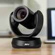 An AVer CAM520 Pro Professional PTZ Conference Camera 1080p by AVer sits on a wooden table, ideal for video conferencing, with a blurred laptop in the background.