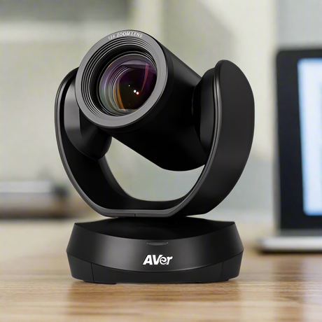 An AVer CAM520 Pro Professional PTZ Conference Camera 1080p by AVer sits on a wooden table, ideal for video conferencing, with a blurred laptop in the background.