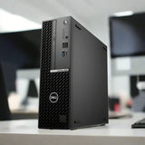 A certified refurbished Dell OptiPlex 7000 SFF i7-12700 2.1GHz 32GB 256GB desktop sits on a white office desk, with blurred monitors and equipment in the background.