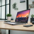 A Dell Precision 3551 i7 10750H mobile workstation with Nvidia Quadro P620 graphics sits on a wooden desk in a modern office, alongside a smartphone, tablet, small plants, and displays a city skyline at sunset.