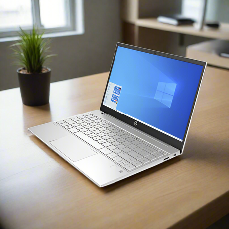 A silver HP Pavilion 13-bb0 i7-1165G7 laptop with 8GB RAM and 512GB SSD sits open on a wooden desk beside a small plant in a bright room, window behind. Certified refurbished, it runs Windows 11 Pro.