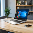 The refurbished HP ProBook 445 G6 Ryzen 7 Pro 2700U (16GB RAM, 512GB SSD, 14", Windows 11 Pro) sits on a wooden desk beside a smartphone, with a blurred bookshelf and potted plant in the background.
