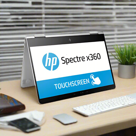 An HP Spectre x360 13-w031tu laptop with a slim aluminum body is set in tent mode on a desk, displaying “HP Spectre x360” and “TOUCHSCREEN” on its 13.3 screen. A keyboard, mouse, and plant are nearby.