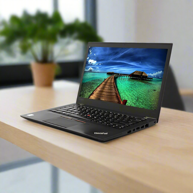 A Lenovo ThinkPad T460s (i7 6600U, 8GB RAM, 256GB SSD, Win10 Pro, 14 Touch) certified refurbished laptop sits on a wooden desk, displaying a tropical beach scene. A potted plant and large window are blurred in the background.