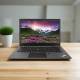 A certified refurbished Lenovo ThinkPad T470s i7 7600U 2.8GHz 8GB 256GB SSD 14 Touch laptop from Lenovo rests on a wooden desk with a potted plant, its screen showing mountains, a vibrant sky, and purple flowers.