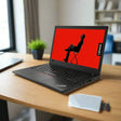 A refurbished Lenovo ThinkPad T480 i5 8350U 1.7GHz 8GB 256GB SSD W11P 14 Touch sits open on a wooden desk, displaying a person on a red background. Nearby are a potted plant, a book, and an external hard drive.
