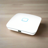 The Open Mesh A62 Tri-Band WiFi Access Point 802.11ac | Wty by Open Mesh, a white enterprise device with a glowing blue square indicator on top and one visible Ethernet port, sits on a light wooden surface.