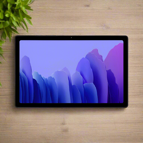 A certified refurbished Samsung Galaxy Tab A7 SM-T505 32GB Tablet Black by Samsung rests on a light wooden surface beside a green leafy plant, displaying a purple and blue abstract wallpaper.