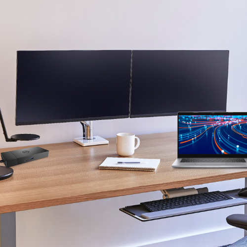 A tidy desk setup includes the Dell Office Bundle: Latitude 5320 i5 Laptop with dual 22 Dell monitors, dock, mount, a notebook with pen, white mug, keyboard, mouse, and a desk lamp.