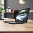 A Dell Latitude 7390 2-in-1 i5 8350U laptop with 8GB RAM and 256GB SSD rests open on a wooden desk, its 13.3 touchscreen showing a scenic wallpaper, while a blurred office with lamp and shelves forms the background.