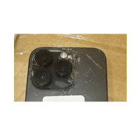 Close-up of a refurbished Apple iPhone 14 Pro 256GB Black Unlocked Smartphone with three camera lenses and cracked back glass, partially covered by scratched plastic film on a cardboard surface. Brand: Apple.