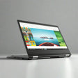 A black Lenovo ThinkPad Yoga 370 (i5 7300U, 8GB RAM, 256GB SSD, 13.3, W10P, NO TOUCH) laptop in tent mode displays colorful travel photos on its screen against a plain gray background.