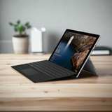 A refurbished Microsoft Surface Pro 4 1724 (i5 6300U, 8GB RAM, 256GB SSD, 12 Touch, Windows 10 Pro) with keyboard sits on a wooden desk. Its display shows scenic wallpaper; a potted plant is blurred in the background.